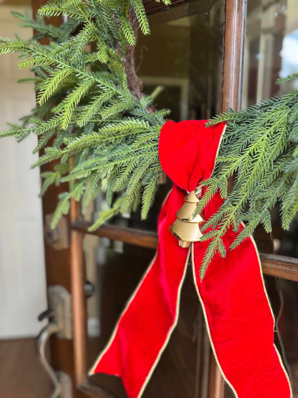 Decorative red bow with a gold Christmas tree ornament on a green wreath 